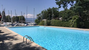 Une piscine à l’eau d’un bleu limpide, entourée d’une terrasse dallée et d’une haie.