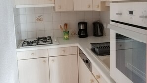 Une cuisine compacte avec des meubles en bois clair, une cuisinière à gaz, une machine à café et un four encastré.