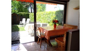 Une terrasse ouverte avec une table et des chaises, un pot de fleurs et une vue sur un jardin et un bâtiment en arrière-plan.