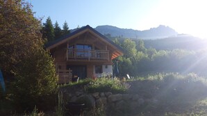 Eine Holzhütte mit Balkon, umgeben von Grün und Bergen.