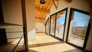 Ein geräumiges Zimmer mit Holzböden, großen Fenstern und einem Balkon.