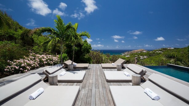 Une terrasse en bois avec quatre chaises longues et une piscine.