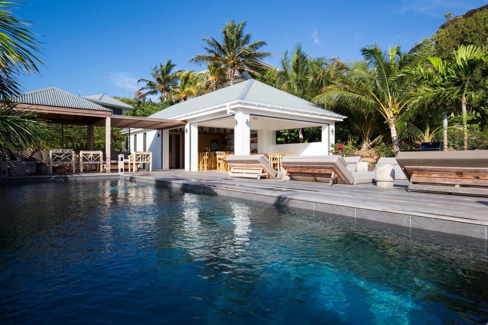 Ein Pool mit Liegestühlen und einer überdachten Sitzgelegenheit, umgeben von Palmen.