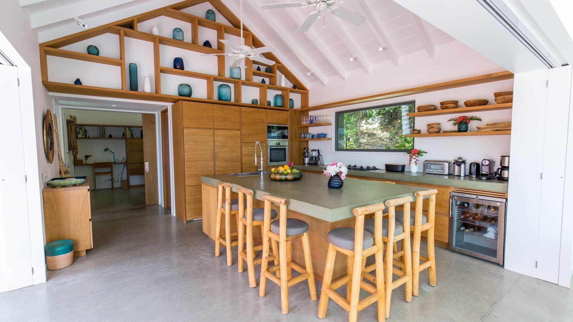 Uma cozinha moderna com ilha central, banquetas de madeira e ventilador de teto.