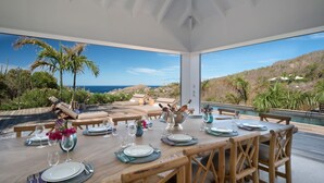 Un coin repas offrant une vue sur l’océan, aménagé avec des meubles en bois et une table dressée pour le repas.