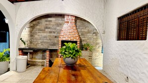 An outdoor dining area with a brick oven, a wooden table, and potted plants. - Beach house with Wi-Fi, pool, and barbecue. (Lucena)
