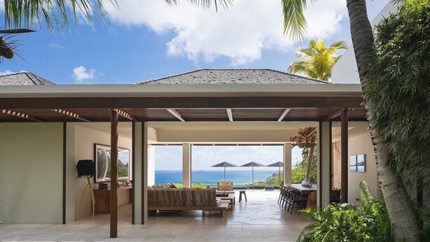 Une maison moderne dotée d’un patio couvert, offrant une vue sur l’océan et agrémentée de plantes tropicales.