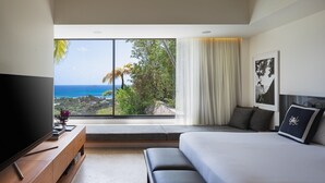Une chambre d’hôtel moderne dotée d’une grande fenêtre offrant une vue panoramique sur l’océan et la végétation.