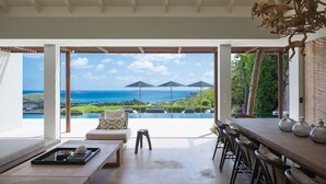 Un salon moderne doté d’une grande porte vitrée donnant sur une piscine et offrant une vue sur l’océan. On y trouve un coin salon avec un canapé et une table basse.