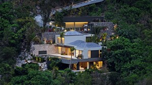 Une maison moderne à plusieurs étages, dotée d’une façade en pierre, de grandes fenêtres et d’une terrasse sur le toit.