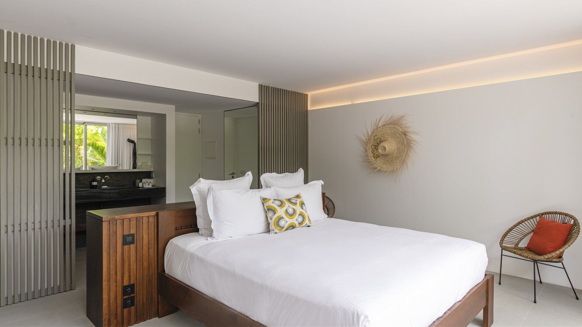 Un dormitorio moderno con una cama grande, un aparador de madera, un tocador con espejo y una silla de mimbre.