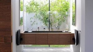 Un bagno moderno con un mobile bagno in legno, una grande finestra e vista sul verde.