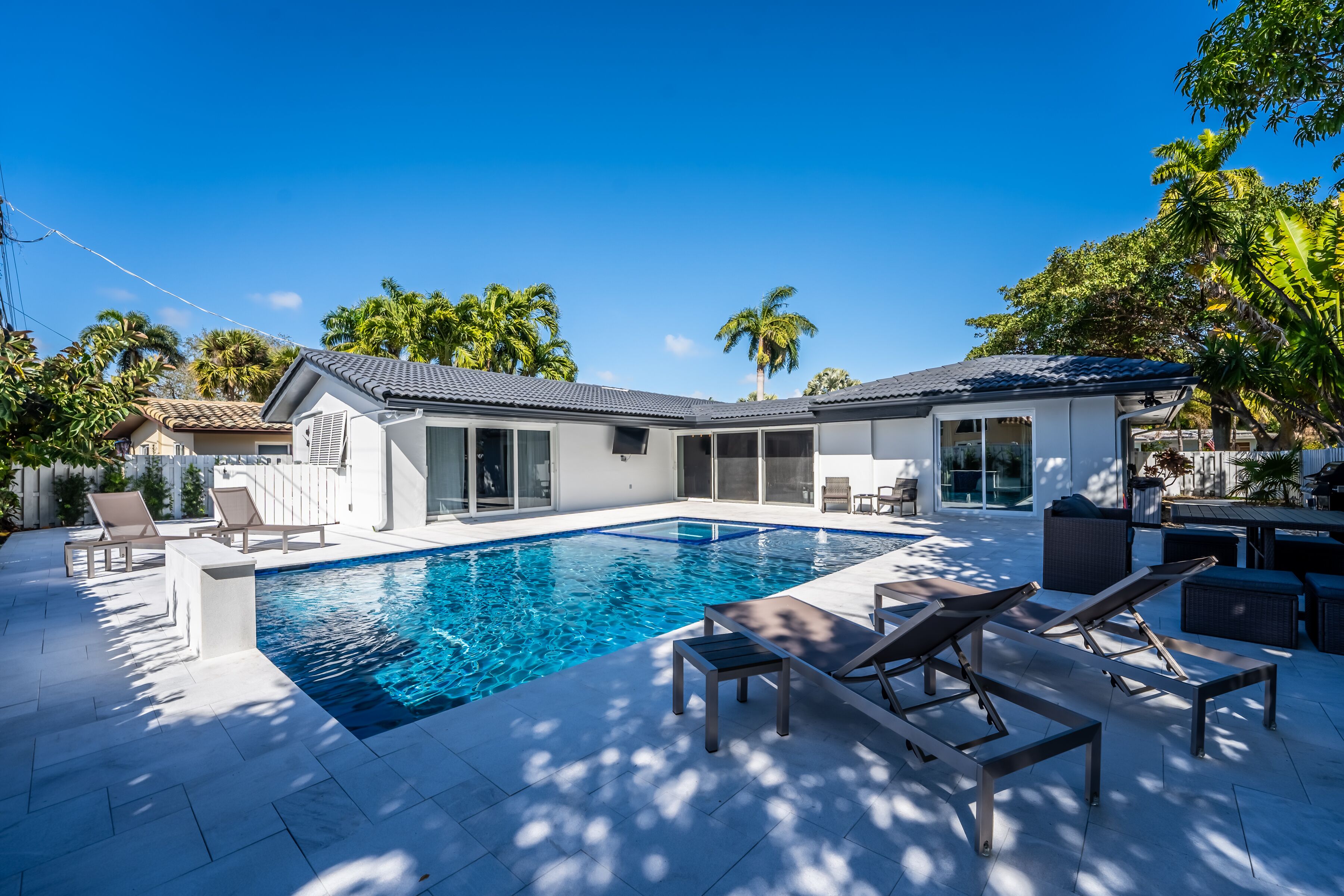A modern house with a swimming pool, outdoor seating, and palm trees.