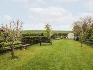 A grassy backyard with a wooden bench, a shed, and a fenced area with trees. - 5 Swinton Mill Farm Cottage (Coldstream)