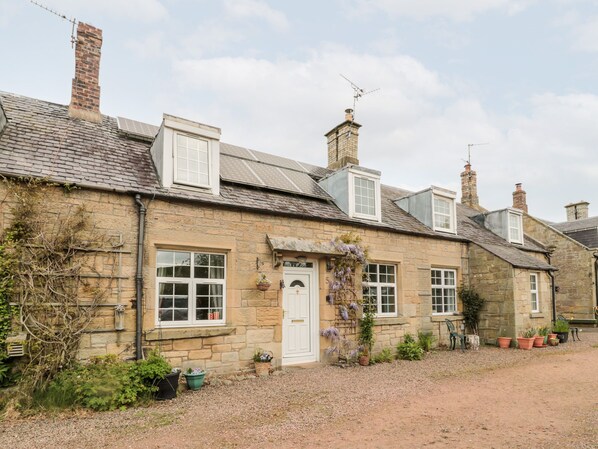 A stone cottage with a gravel driveway, white door, and multiple chimneys. - 5 Swinton Mill Farm Cottage (Coldstream)