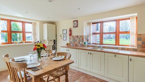 A kitchen with a dining table set for four, white cabinets, a window with a view of the outdoors, and a clock on the wall. - The Parlour - UK37517 (Routh, Beverley)