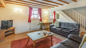A cozy living room with a wooden ceiling, a sofa, a coffee table, a TV on a wooden stand, and a staircase. - The Parlour - UK37517 (Routh, Beverley)