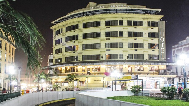 Un hotel de varios pisos con fachada curva, varios balcones y una entrada bien iluminada.
