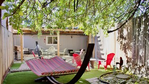 A hammock under a tree, red chairs, and a garden area with rocks and a brick path.