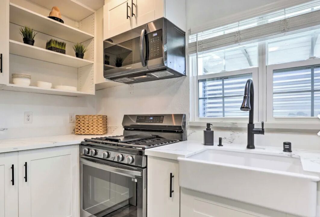 Una cocina moderna con armarios blancos, electrodomésticos de acero inoxidable y una ventana con persianas.