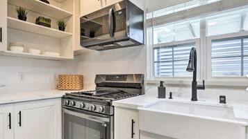 Una cocina moderna con armarios blancos, electrodomésticos de acero inoxidable y una ventana con persianas.