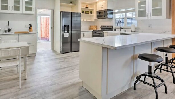 A modern kitchen with white cabinetry, a central island with stools, a stainless steel refrigerator, and a built-in oven.