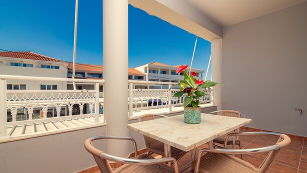 Ein Balkon mit Tisch und Stühlen, einem Blumentopf und Blick auf Gebäude.