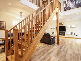 A wooden staircase leading to a living area with a flat-screen TV, a fireplace, and a dining table.