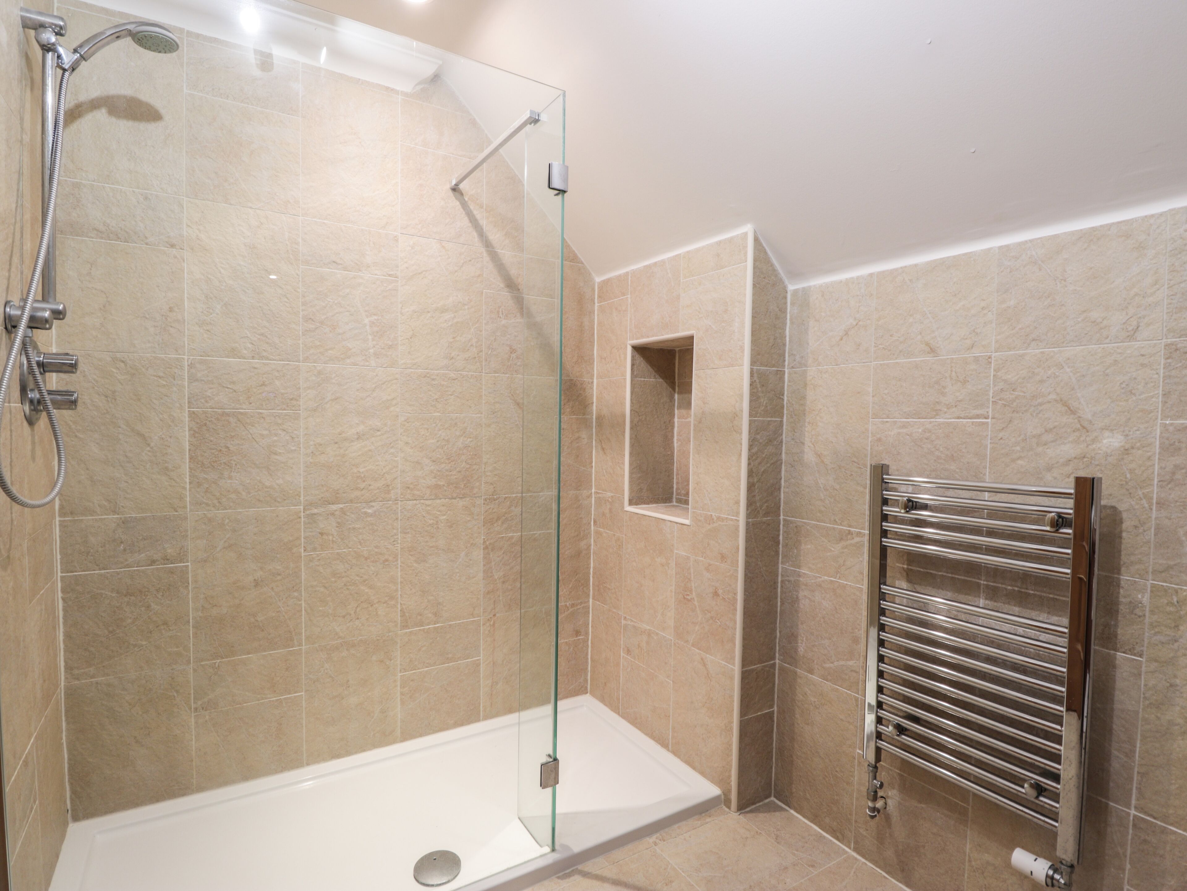 A modern bathroom with a glass-enclosed shower, a white bathtub, and a built-in towel rack.