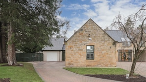 A stone building with a garage, a paved driveway, and a well-maintained lawn. - 1 The Coach House (Elgin)