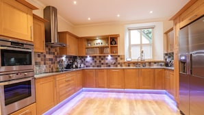 A modern kitchen with wooden cabinets, stainless steel appliances, and a tiled backsplash. - 1 The Coach House (Elgin)