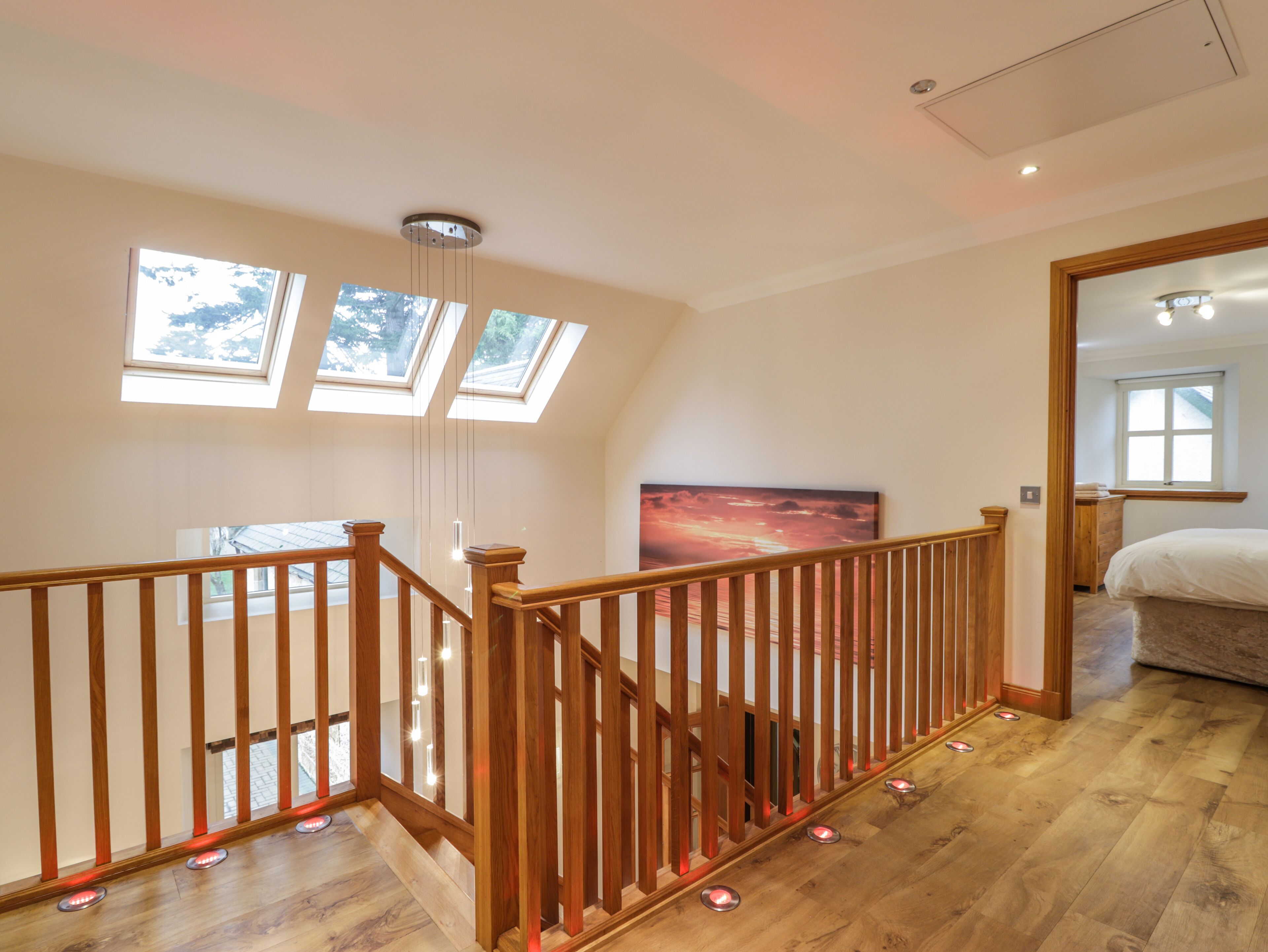 A spacious room with a wooden staircase, skylights, and a large painting on the wall.