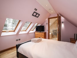 A bedroom with a bed, a TV, a wooden dresser, a mirror, and skylights.