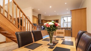 A dining area with a wooden table, black placemats, and leather chairs. A vase with flowers is on the table. - 1 The Coach House (Elgin)