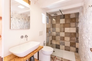 A bathroom with a white sink, a wooden countertop, a white toilet, and a shower with a checkered tile wall. - I trulli di Emma (Alliste)