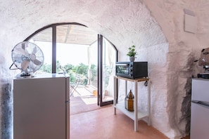 A compact kitchen with a fan, microwave, and a small shelf with a plant. - I trulli di Emma (Alliste)