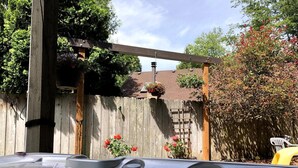 Ett bubbelbad i en trädgård med ett trästaket, en pergola och en gul stol.