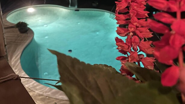 En swimmingpool med en fontän, omgiven av en terrass och ett hus i bakgrunden.