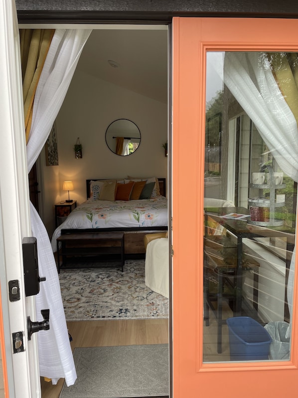 A bedroom with a bed, a bedside table, a lamp, a mirror, and a window with curtains.