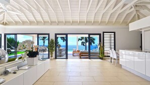 A modern kitchen with white cabinets, a large island, and a view of the ocean through glass doors. - Enzuma (2/3 Rooms) Luxury villa (Toiny)