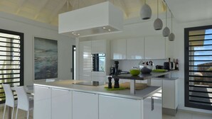 A modern kitchen with white cabinetry, a central island, and pendant lighting. - Enzuma (2/3 Rooms) Luxury villa (Toiny)