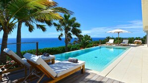 Ein Poolbereich mit Liegestühlen, einer Holzterrasse und Blick auf das Meer.