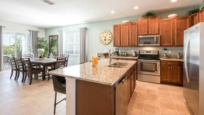 Una cocina moderna con encimeras de granito, electrodomésticos de acero inoxidable, armarios de madera y un comedor con mesa y sillas.