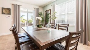 Un comedor con una mesa rectangular, seis sillas y vistas al exterior a través de amplios ventanales con cortinas.