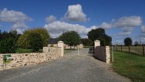 A gated entrance with a stone wall and a metal gate, leading to a building with a sloped roof. - FAMILY HOME, former farmhouse with exceptional views. (Pommerieux)