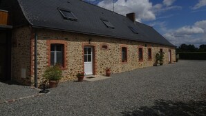 A stone building with a sloped roof, multiple windows, and a gravel driveway. - FAMILY HOME, former farmhouse with exceptional views. (Pommerieux)