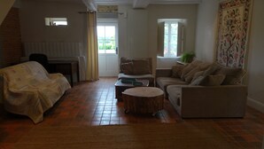 A cozy living room with a sofa, a round coffee table, and a chair. There is a window with a view of greenery outside. - FAMILY HOME, former farmhouse with exceptional views. (Pommerieux)