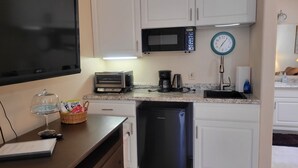 Una cucina compatta con mobili bianchi, un forno a microonde, un tostapane, una macchina per il caffè e una lavastoviglie.