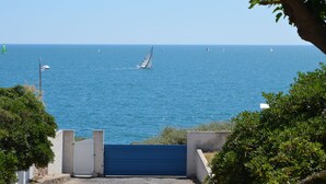 Udsigt over kysten med et klart, blå hav, en sejlbåd og en blå port, der fører til stranden.