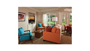A spacious living room with a large window, a television, and a dining area with red chairs. - Marriott's Desert Springs Villas II Resort (Palm Desert)